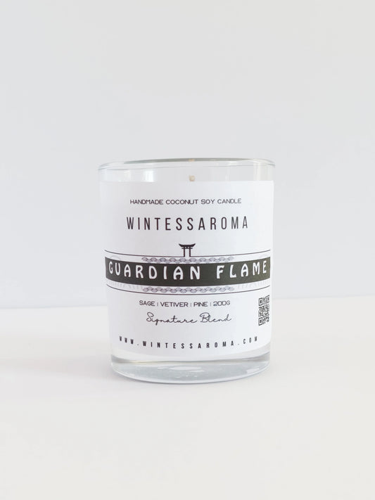 A clear glass candle with a label that reads 'WINTESSARAOMA GUARDIAN FLAME' The candle is placed on a white surface against a white background.