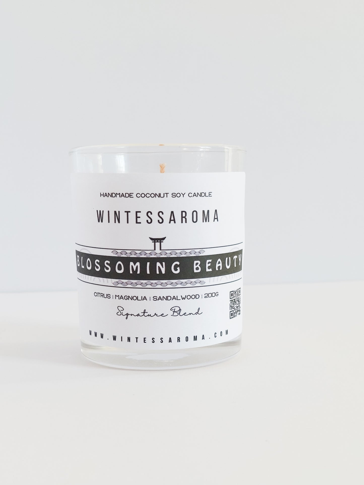 A clear glass candle with a label that reads 'Wintessaroma Blossoming Beauty Korean Tale'. The candle is placed on a white surface against a white background.