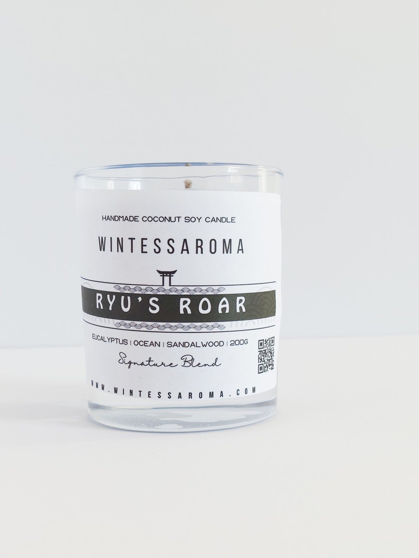 A clear glass candle with a white label that reads 'Wintessaroma' and 'Ryu's Roar'. The label includes the scent notes of citrus and eucalyptus.