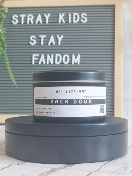 Candle labeled 'Back Door' by Wintessaroma on a stand with a letterboard in the background. Front View