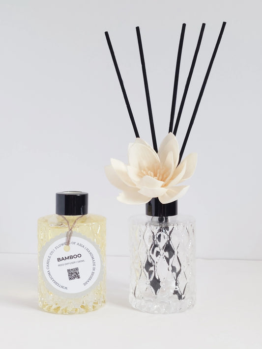 Two clear reed diffusers with bamboo-scented oil and several bamboo reeds, alongside a smaller bottle of the same scent.