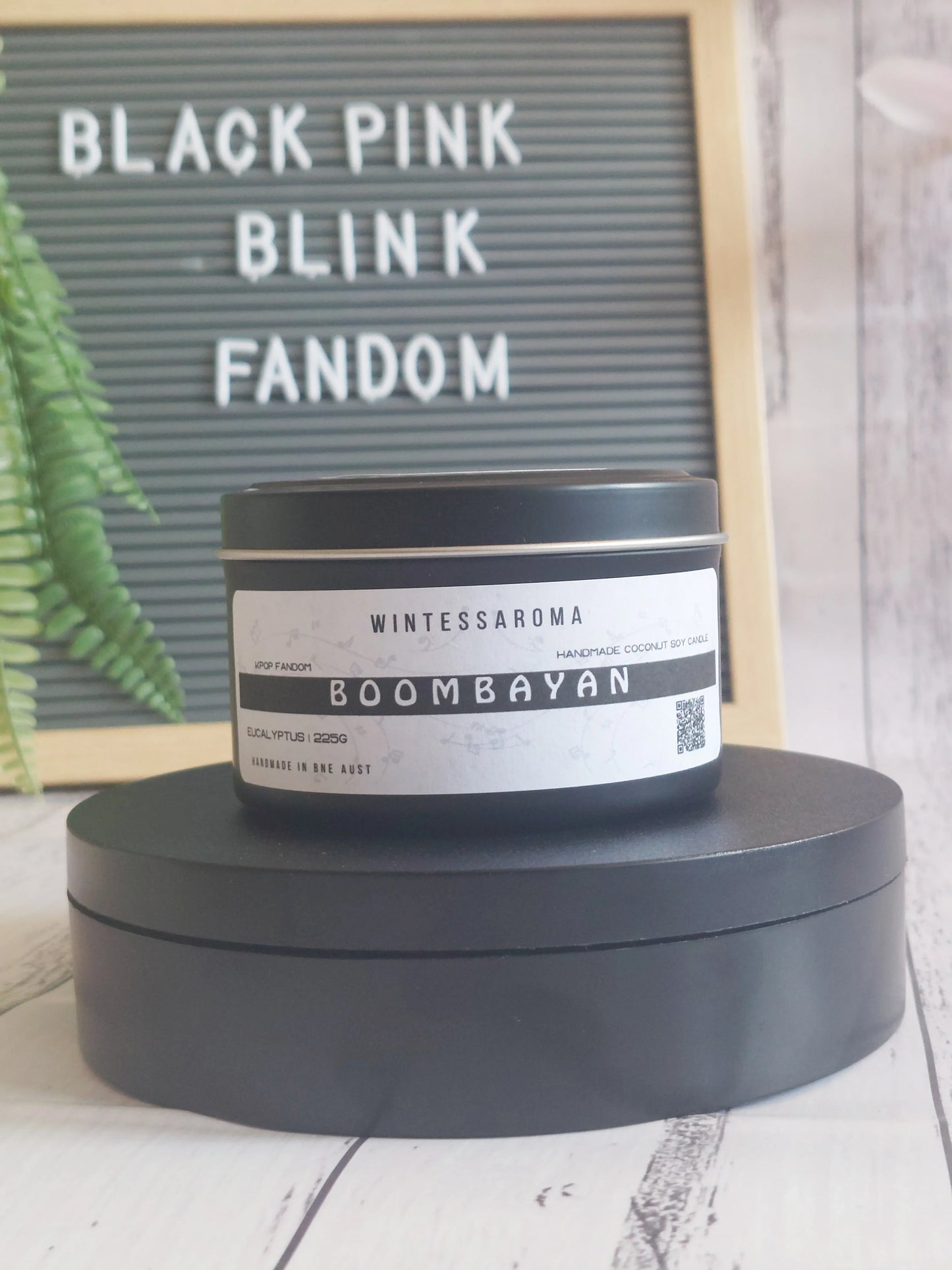 Candle labeled 'Boombayan' by Wintessaroma on a black stand with a letterboard in the background. Front View