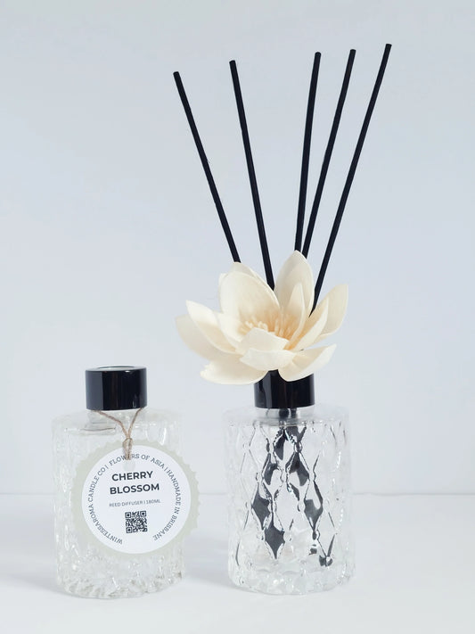 A beige reed diffuser with a white flower and a black spray bottle labeled 'Cherry Blossom'.