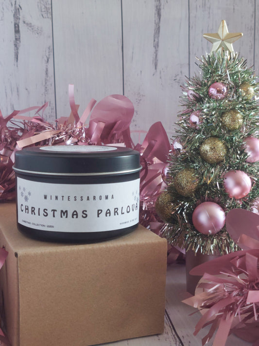 Candle labeled 'Christmas Parlour' with a small decorated tree and pink tinsel on a wooden surface.