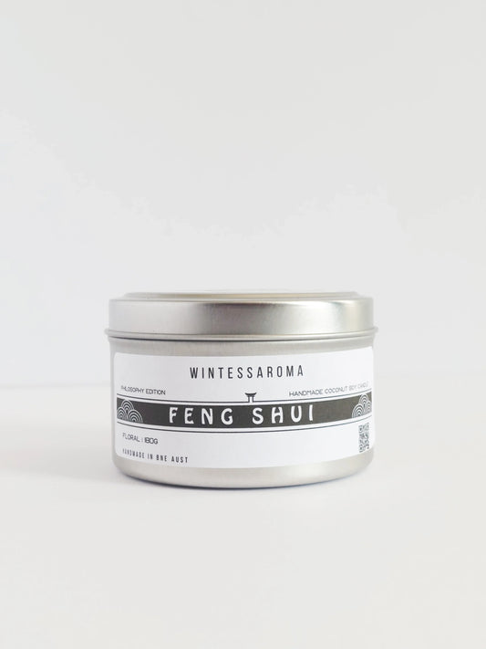 A cylindrical metal candle with a white label that has 'Wintessaroma FENG SHUI' written on it, placed against a white background.