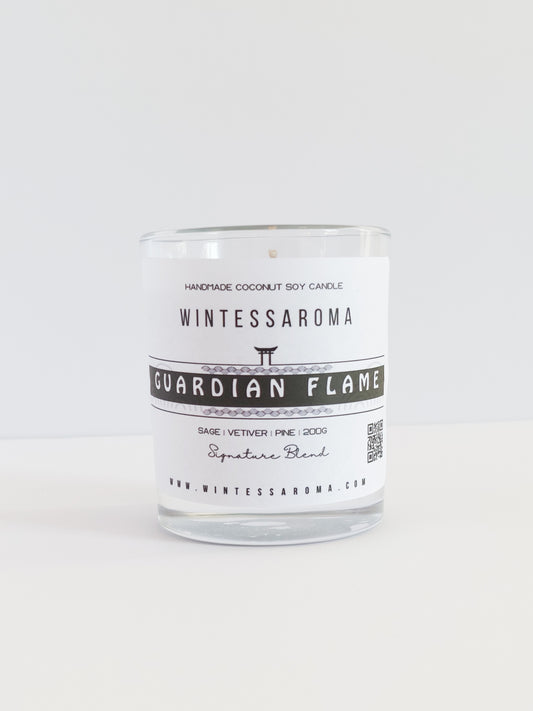 A clear glass candle with a label that reads 'WINTESSARAOMA GUARDIAN FLAME' The candle is placed on a white surface against a white background.