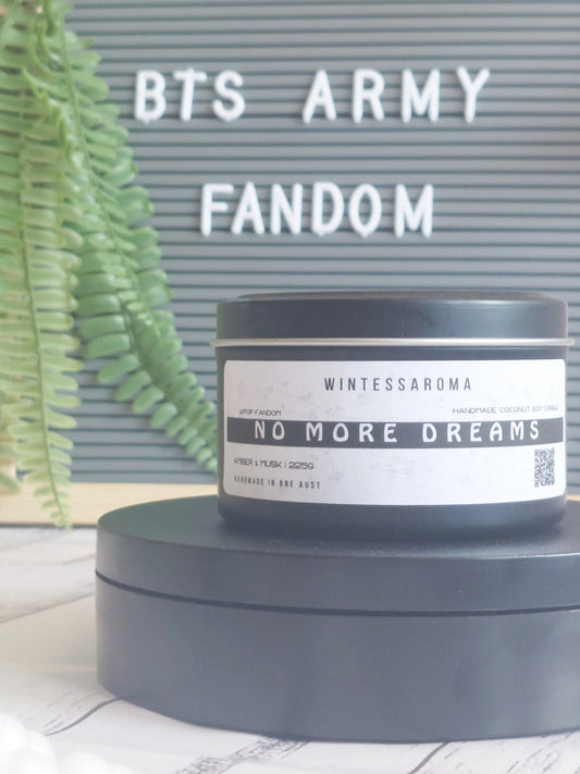 Candle labeled 'No More Dreams' by Wintessaroma with a BTS Army Fandom sign in the background. Front close up view. 