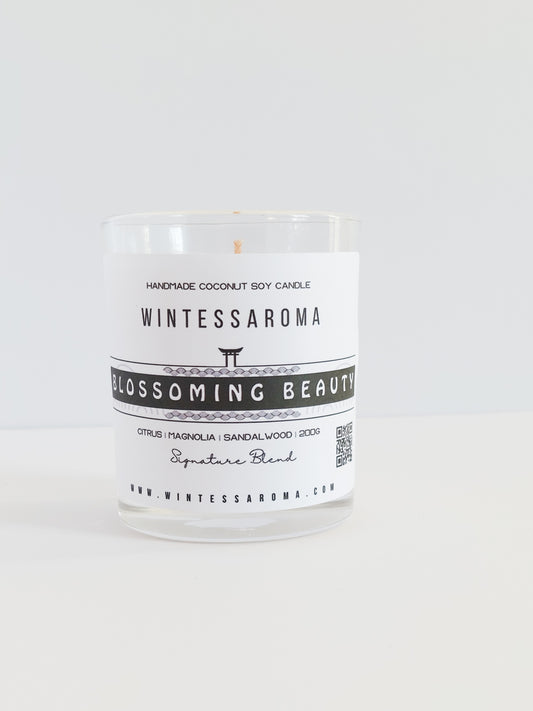 A clear glass candle with a label that reads 'Wintessaroma Blossoming Beauty Korean Tale'. The candle is placed on a white surface against a white background.