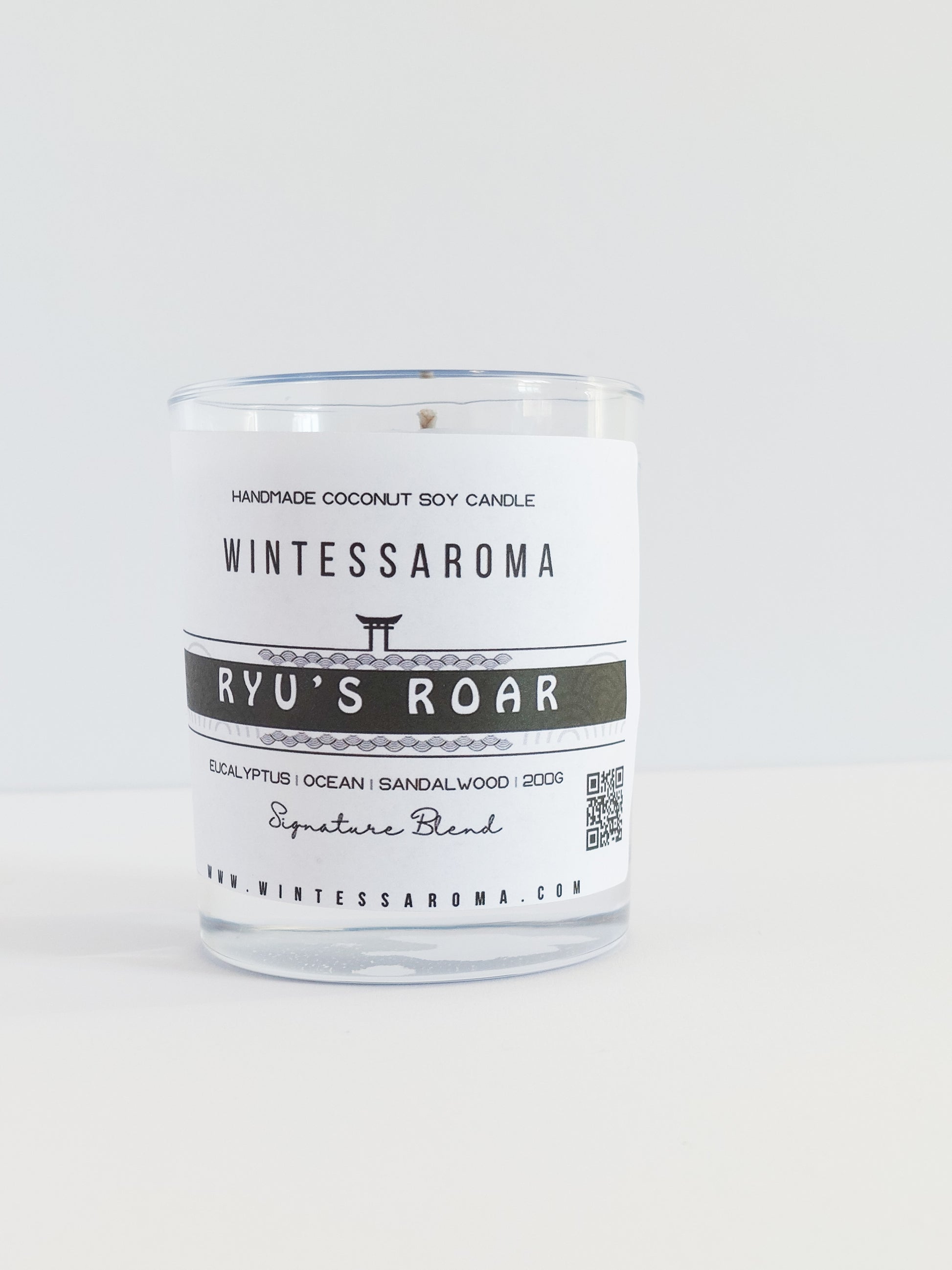 A clear glass candle with a white label that reads 'Wintessaroma' and 'Ryu's Roar'. The label includes the scent notes of citrus and eucalyptus.