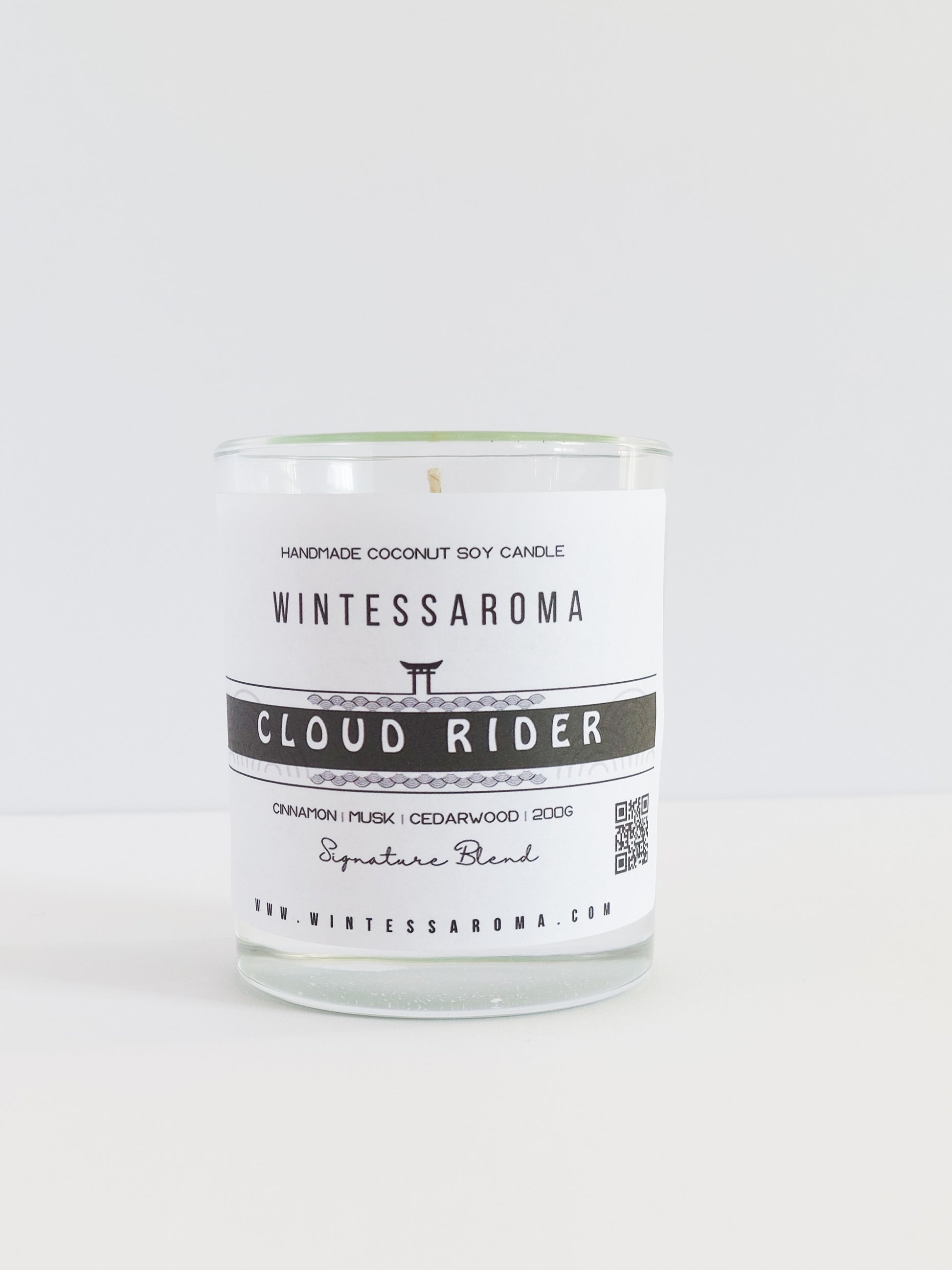 A clear glass candle with a label that reads 'WINTESSAROMA CLOUD RIDER' along with some additional text that includes the scent notes of the candle.
