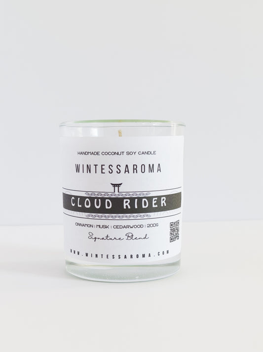 A clear glass candle with a label that reads 'WINTESSAROMA CLOUD RIDER' along with some additional text that includes the scent notes of the candle.