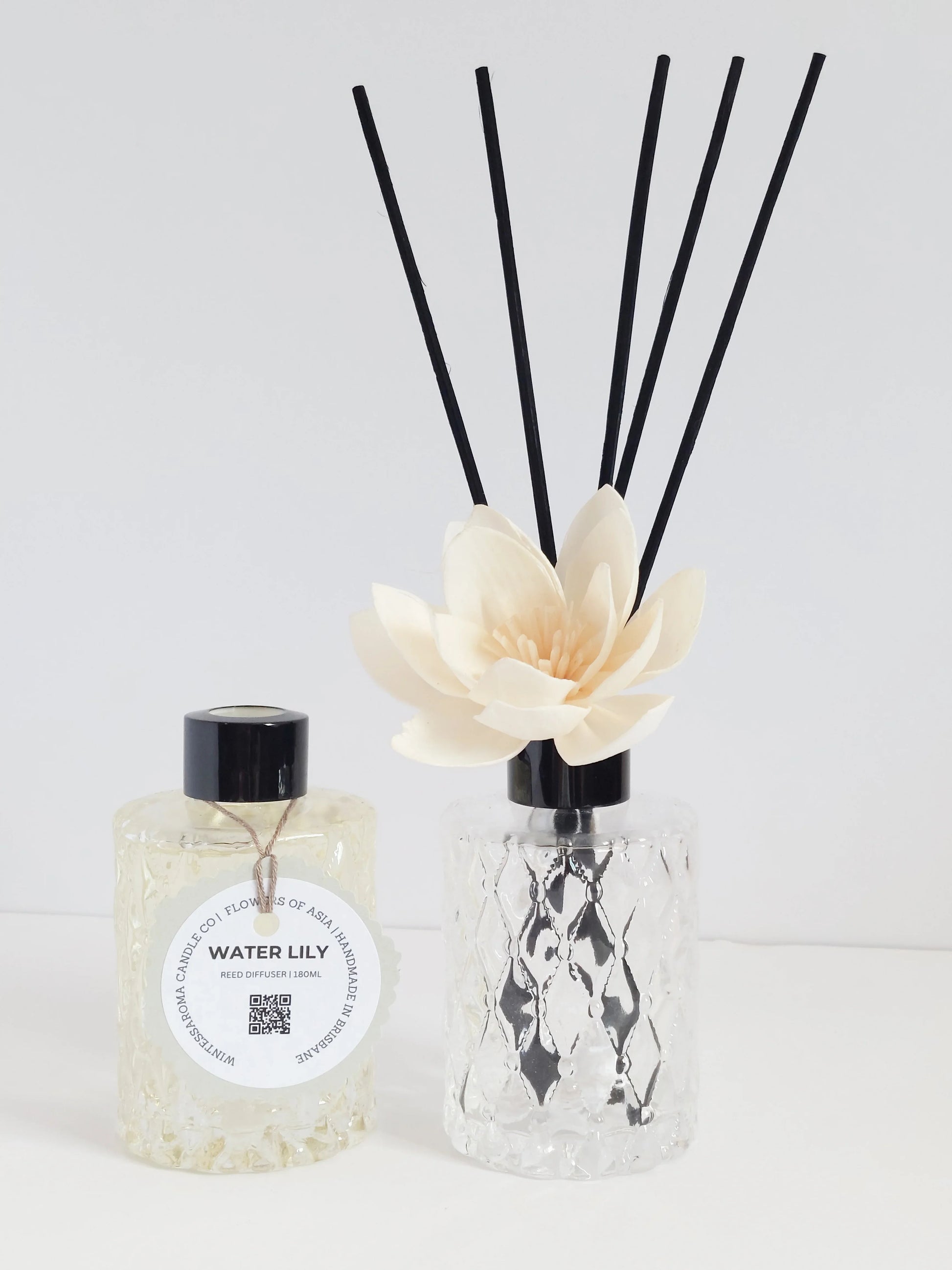 A reed diffuser with clear sticks and a room spray bottle, both with a floral design, arranged with a decorative flower.