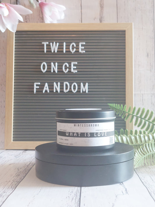 Candle labeled 'What is Love' on a stand with a letterboard reading 'TWICE ONCE FANDOM' in the background. Front View